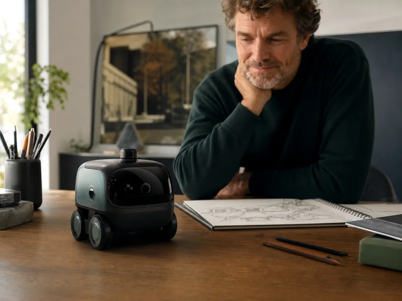 Créatif observant un petit robot de bureau autonome générique explorer son espace de travail